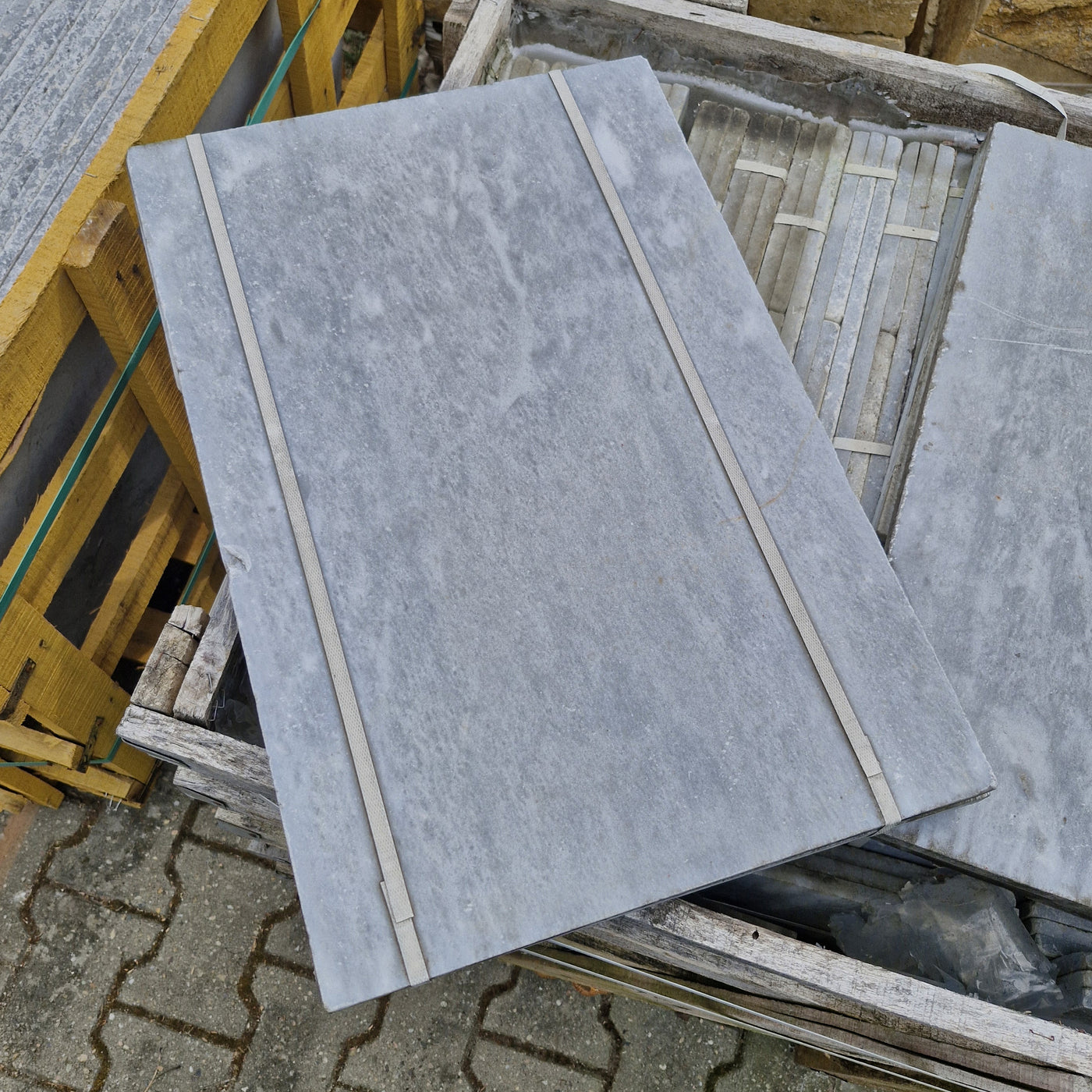 Helle getrommelte Marmorfliesen von CAMELIA, Naturstein, quadratisch, Oberfläche mit natürlicher Maserung, liegend auf einem Boden.